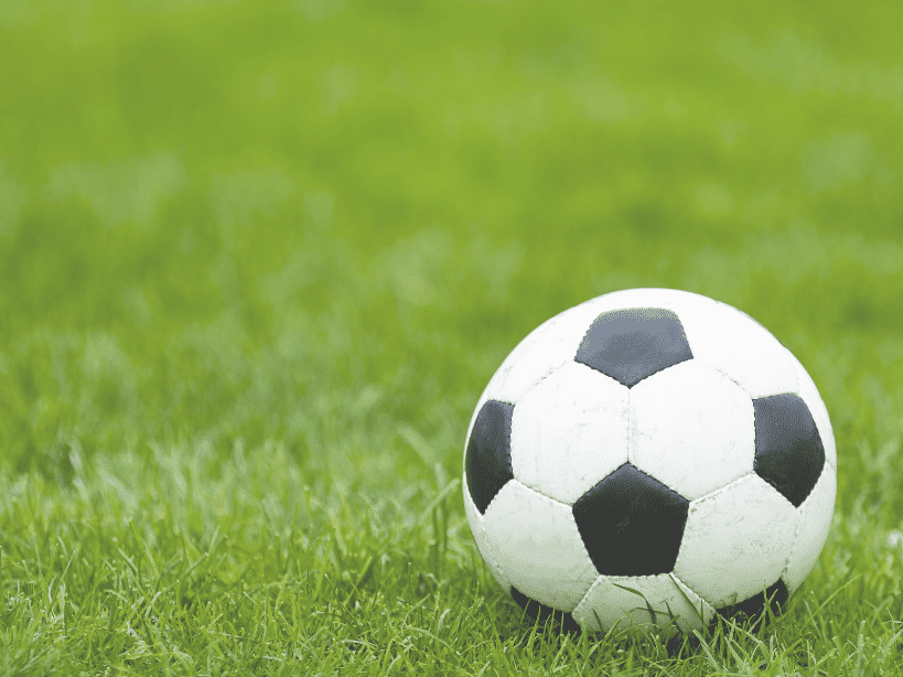 Ein Fußball liegt auf grünem Rasen, gut sichtbar im Vordergrund der Aufnahme.