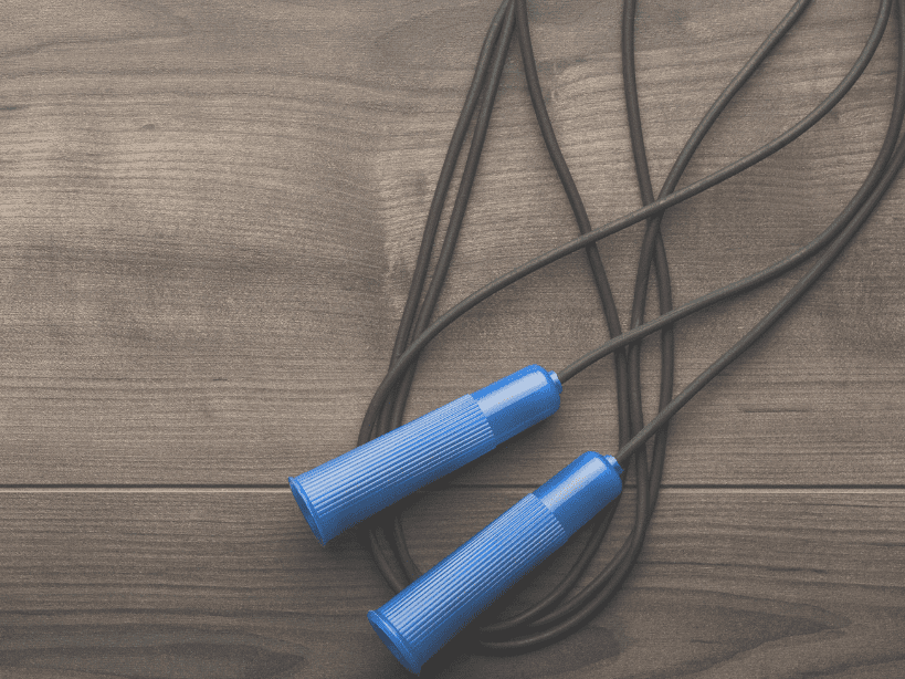 Springseil mit blauen Griffen auf einer Holzoberfläche, in einer lockeren Schlaufe liegend.