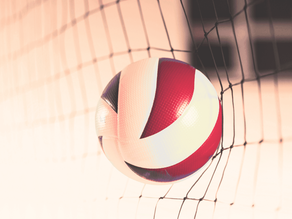 Nahaufnahme eines Volleyballs, der im Netz hängt, mit rot-weißer Farbgebung auf einem blassen Hintergrund.