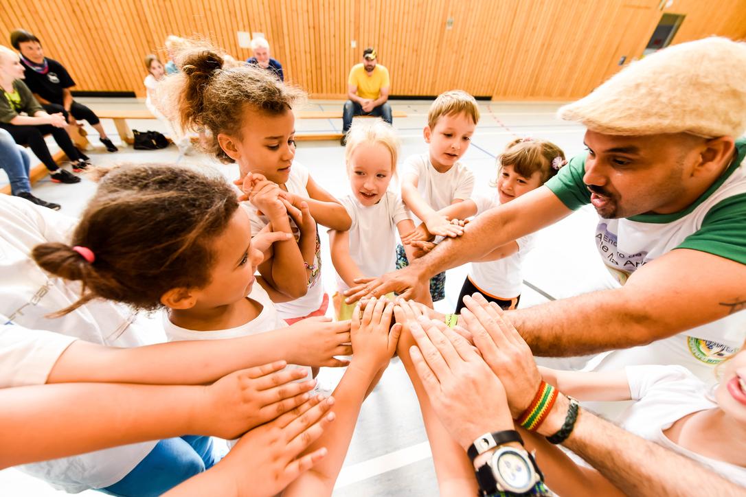 Gruppenspiel mit Kindern, die ihre Hände zum gemeinsamen Aufeinandertreffen heben, unter Anleitung eines Erwachsenen.