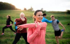 Large group of fit and active people stretching after doing exercise in nature.