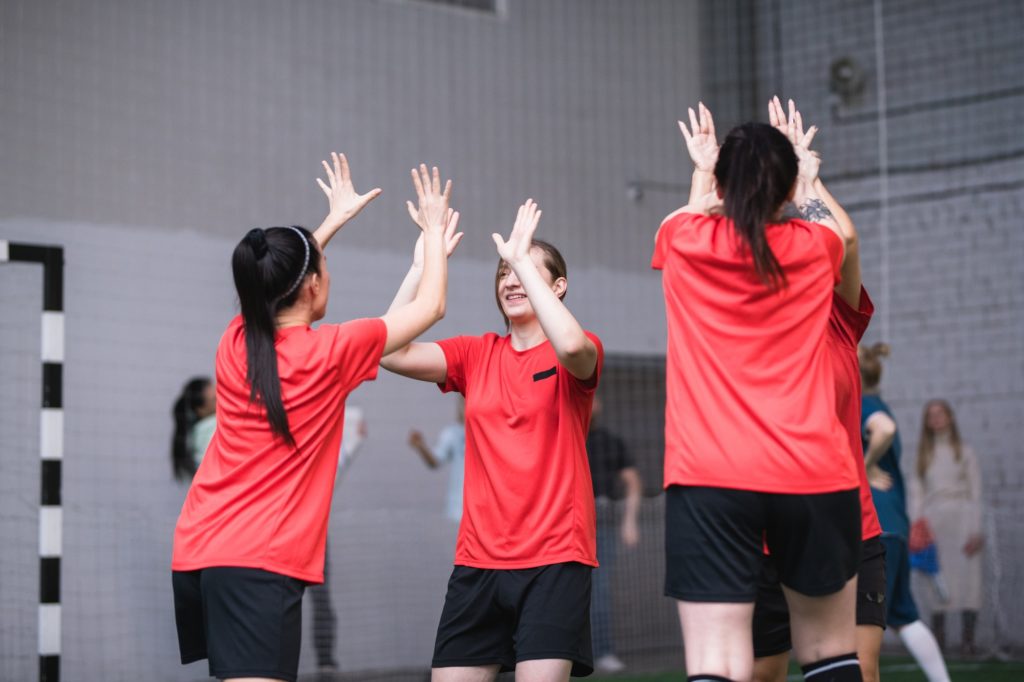 Team of active girls in sports uniform expressing triumph by high-five gesture